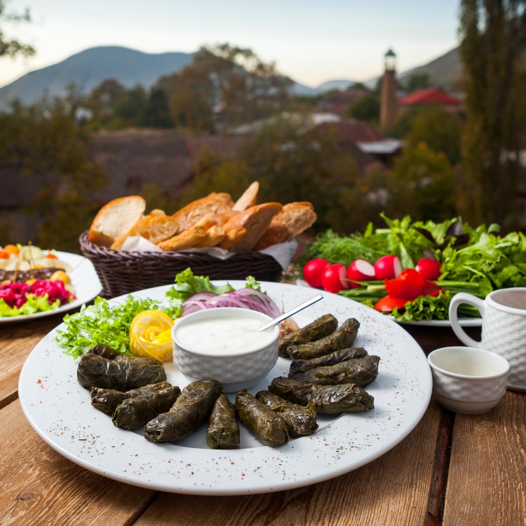 Armenian picnic table with dolma, fresh herbs, bread, and vegetables served outdoors in the mountains.